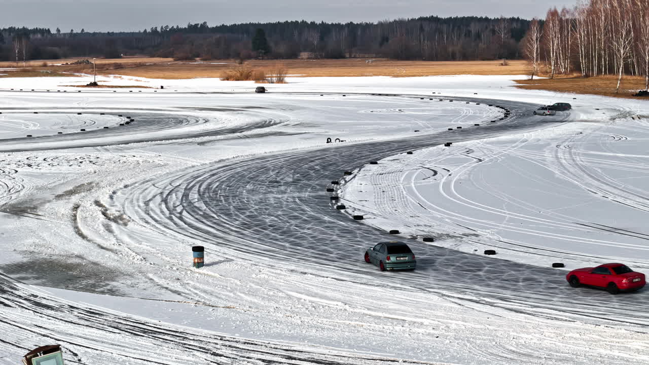Multiple cars carve intricate paths and loops on a snow-covered field, turning a frozen landscape into a dynamic playground of tire tracks and drifts