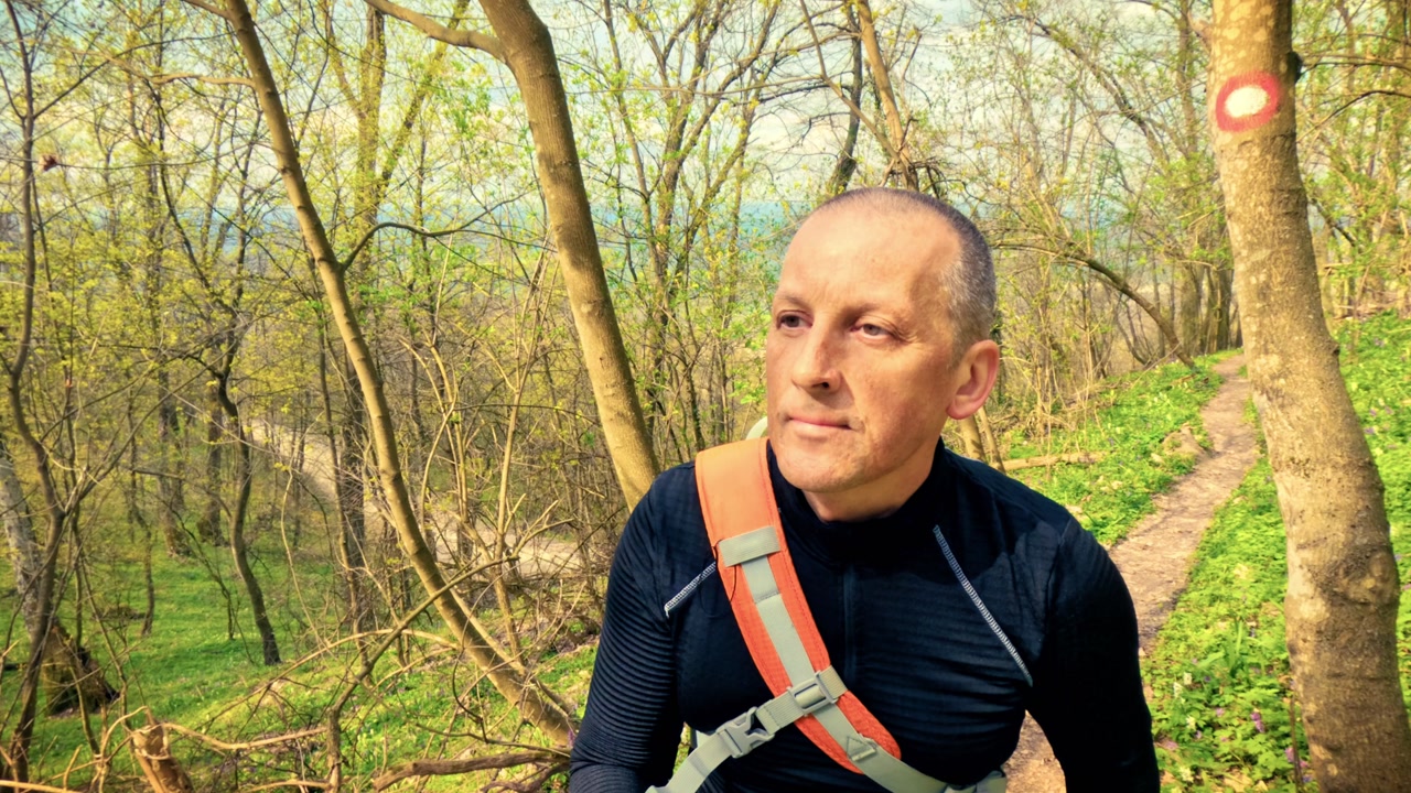 Authentic mature man walking through a blooming spring woodland path with purple flowers. Promoting personal health, fitness, mental well-being, and the calming power of nature for stress relief.