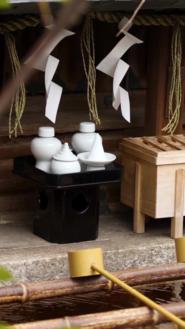 Static shot of ceramic offerings, paper streamers, and bamboo ladles at a Japanese shrine.