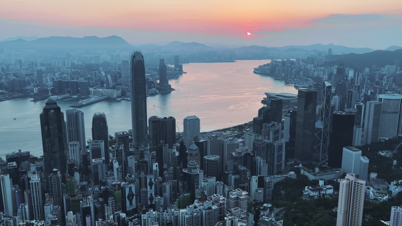 Cinematic aerial view of Hong Kong skyline shrouded in mist at blue hour, with glowing skyscrapers and Victoria Harbour fading into a moody, atmospheric twilight
