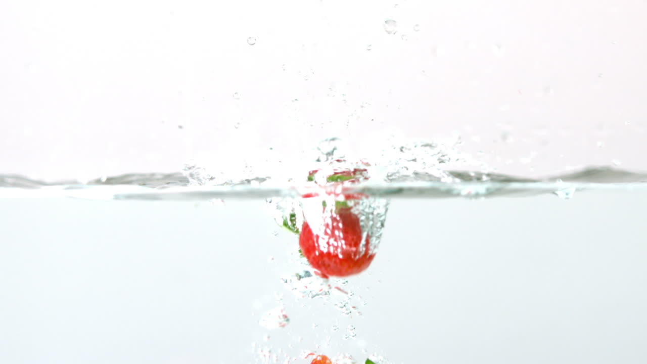 fresas cayendo en el agua sobre un fondo blanco