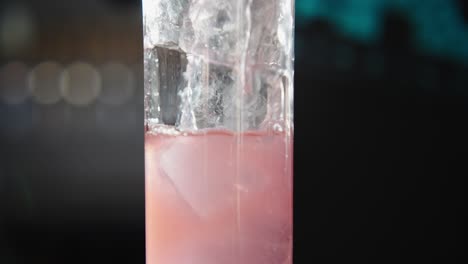 bartender pouring pink liquid into an ice-filled glass slowly