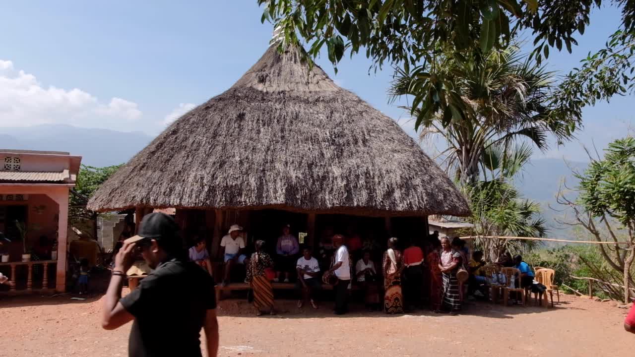 A remote Timorese family and village community sitting at traditional thatched roof sacred house in Timor Leste, Southeast Asia