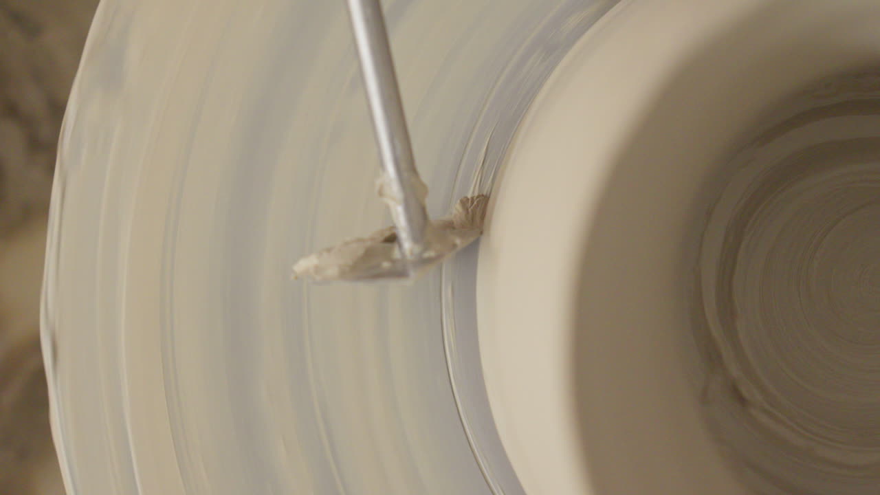 Artisan masterfully completes a vase on a potter's wheel, using tool to refine the shape and achieve a flawless finish of the bottom