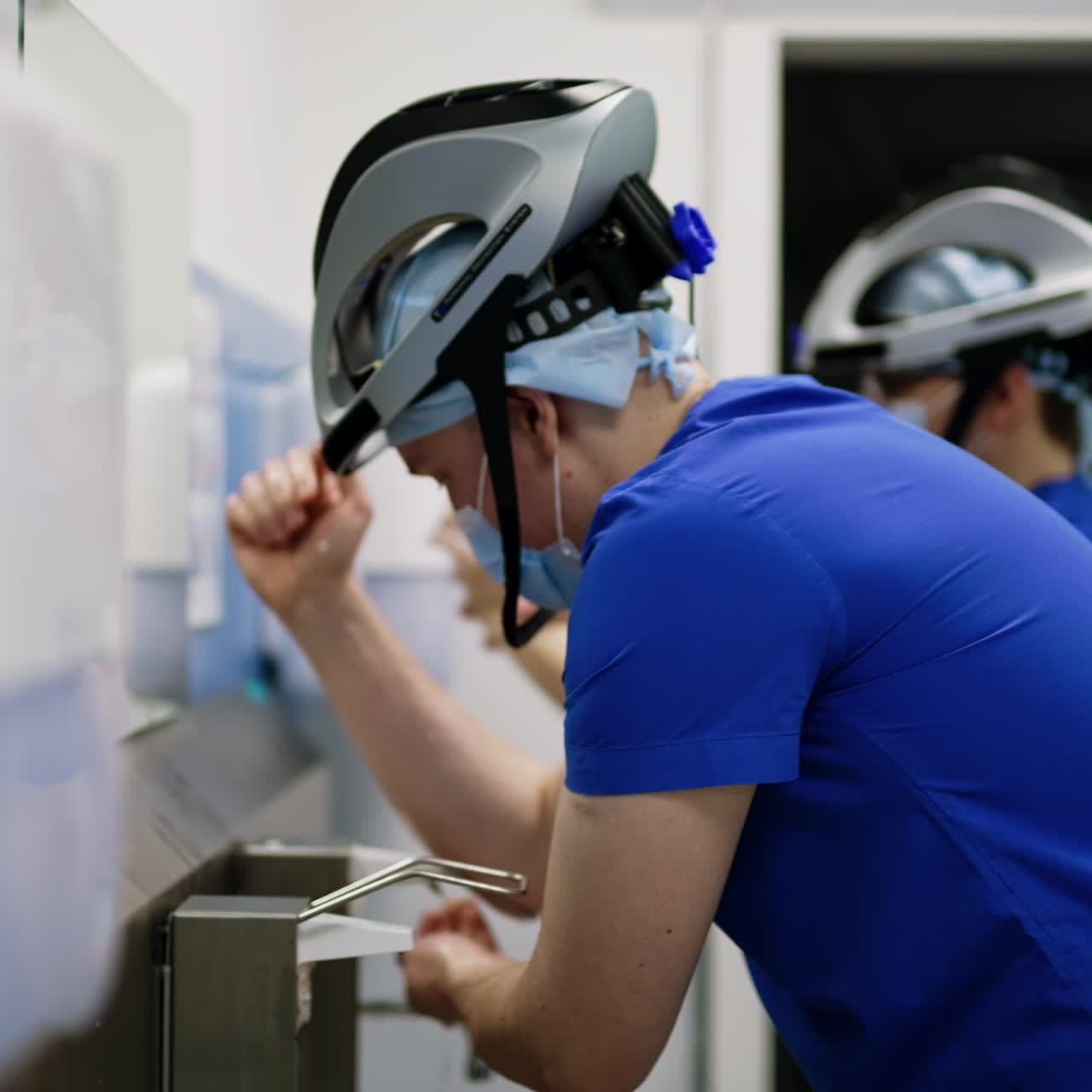 Caucasian male doctor wearing mask, helmet and uniform side view. Portrait of a surgeon carefully washing hands preparing for the surgery
