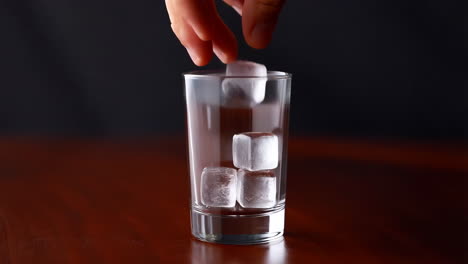 hand dropping ice cubes into a glass