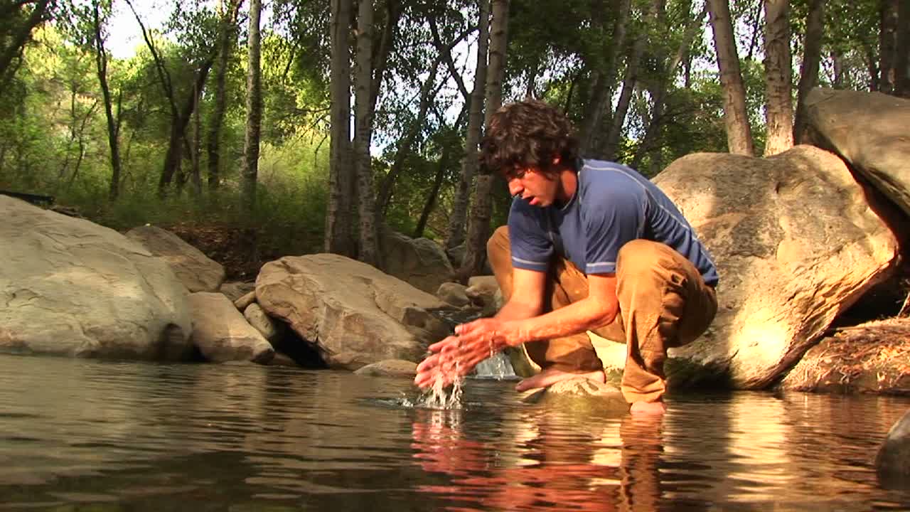 ángulo bajo de un excursionista lavándose la cara en una piscina de montaña
