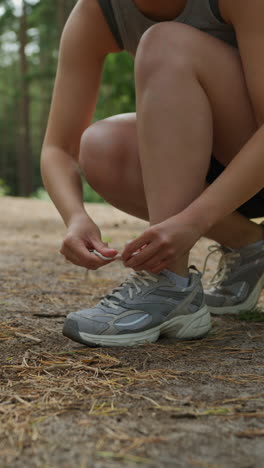 video vertical de cerca de una mujer atando los cordones de su zapato de entrenamiento antes de hacer ejercicio corriendo por la pista a través del bosque disparado en tiempo real 1