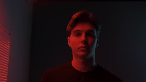 close-up portrait of a young man in a dark studio lit with red lights.