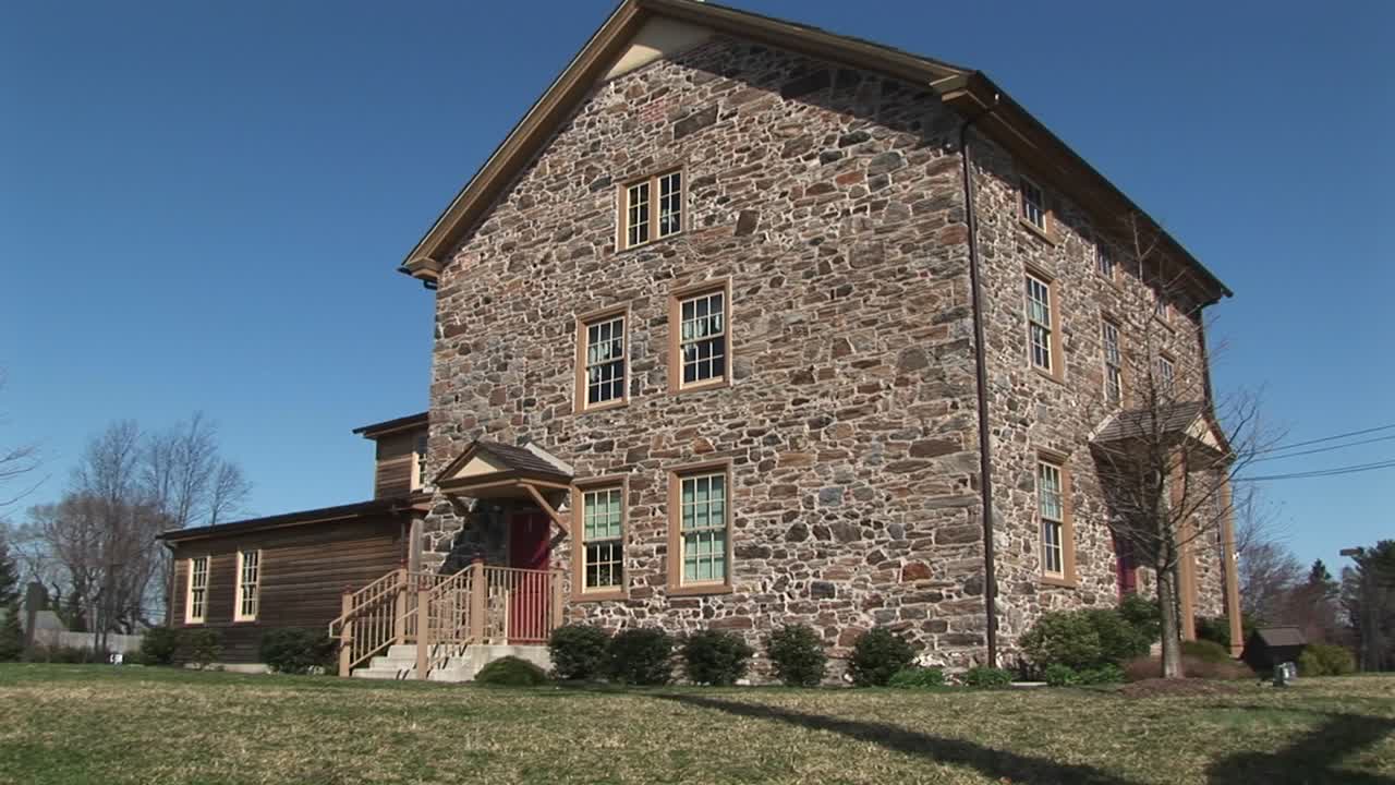 카메라가 3층 필드스톤 하우스를 확대하여 지상 창문과 빨간색 현관문에 초점을 맞춥니다.