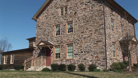 the camera zooms in on threestory fieldstone house to focus on ground level windows and red front door