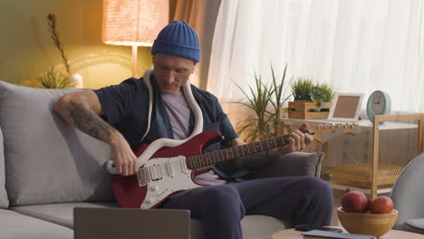 man sitting on a sofa and holding a snake around his neck while playing the electric guitar