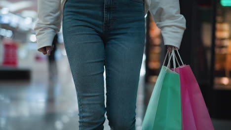 pink shopping bag held in a lady's hand with polished nails, complemented by a mint-colored bag, set against a vibrant shopping mall background with modern displays and glowing ambient lighting