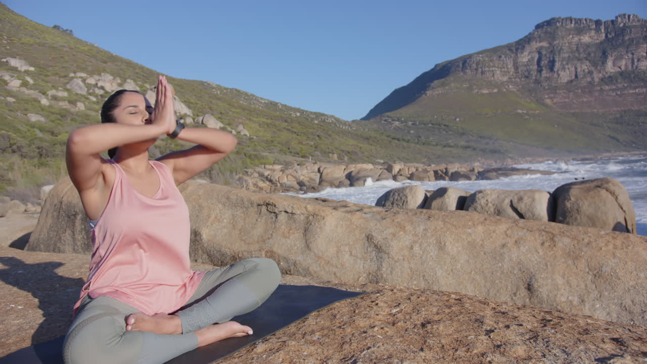 Sitting cross-legged on rock near ocean, asian woman meditating outdoors
