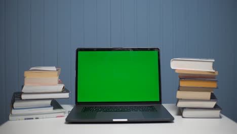una computadora portátil de pantalla verde sentada en un escritorio de tareas con libros.