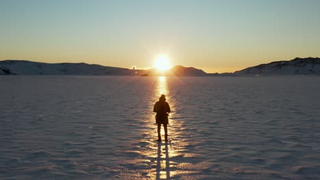 Push-In-Fly-Over-Silhouetted-Man-in-Sunray-on-Snow-Covered-Frozen-Lake