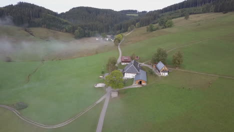 Aerial-flyover-of-quaint-old-farmhouses-in-foggy-green-German-valley