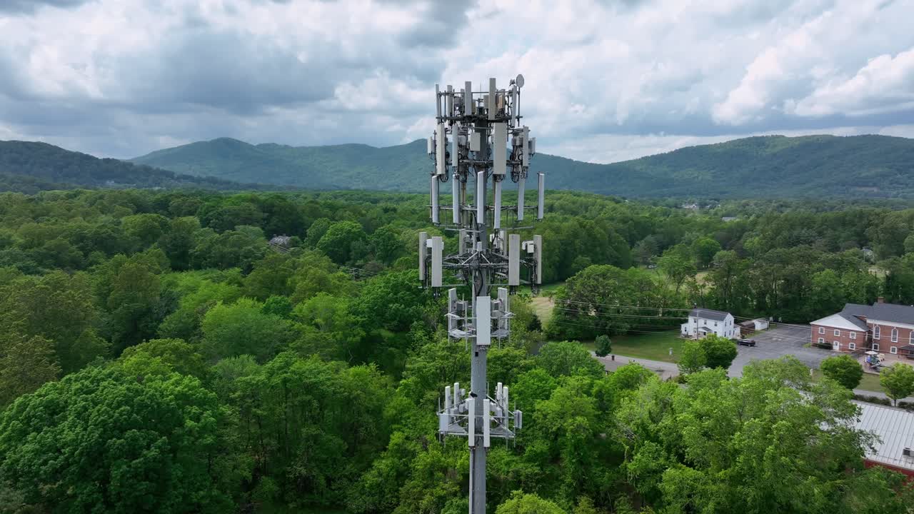 Telecommunication Tower in Suburb district of american town. Cellular Network Antenna sending Signal Waves to neighborhood. Aerial close up orbit. Cloudy day in forest landscape with hills in USA.