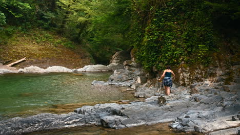 mujer caminando a través de un río del bosque