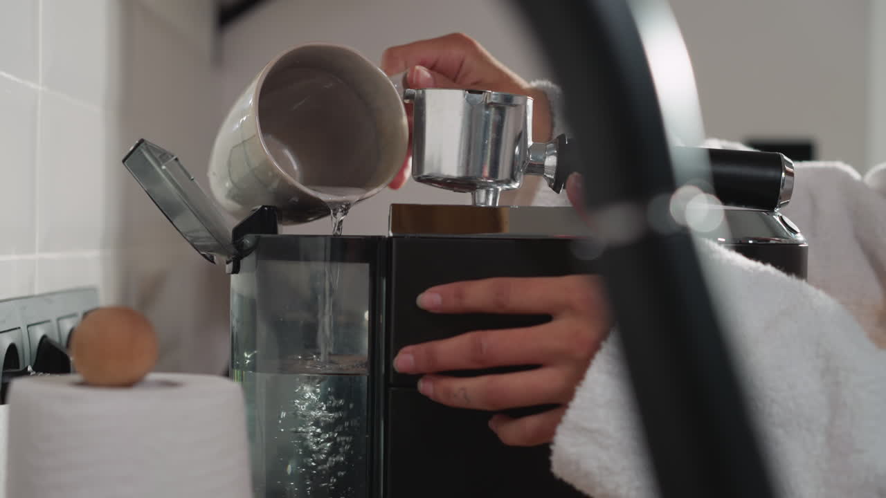 женщина наполняет резервуар кофейной машины водой вблизи. женщина наливает воду из чашки в резервуар производителя для приготовления энергетического напитка. техническое обслуживание современного устройства