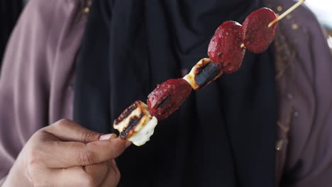 primer plano de un pinchazo de queso a la parrilla y salchichas sostenido por una mujer