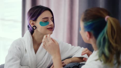 two domestic women at home applying patches under eyes to each other