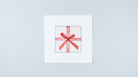 4k drawing of gift box in craft paper tied with red ribbon appears on white piece of paper. then hands take real gift in place of painted one. grey background.