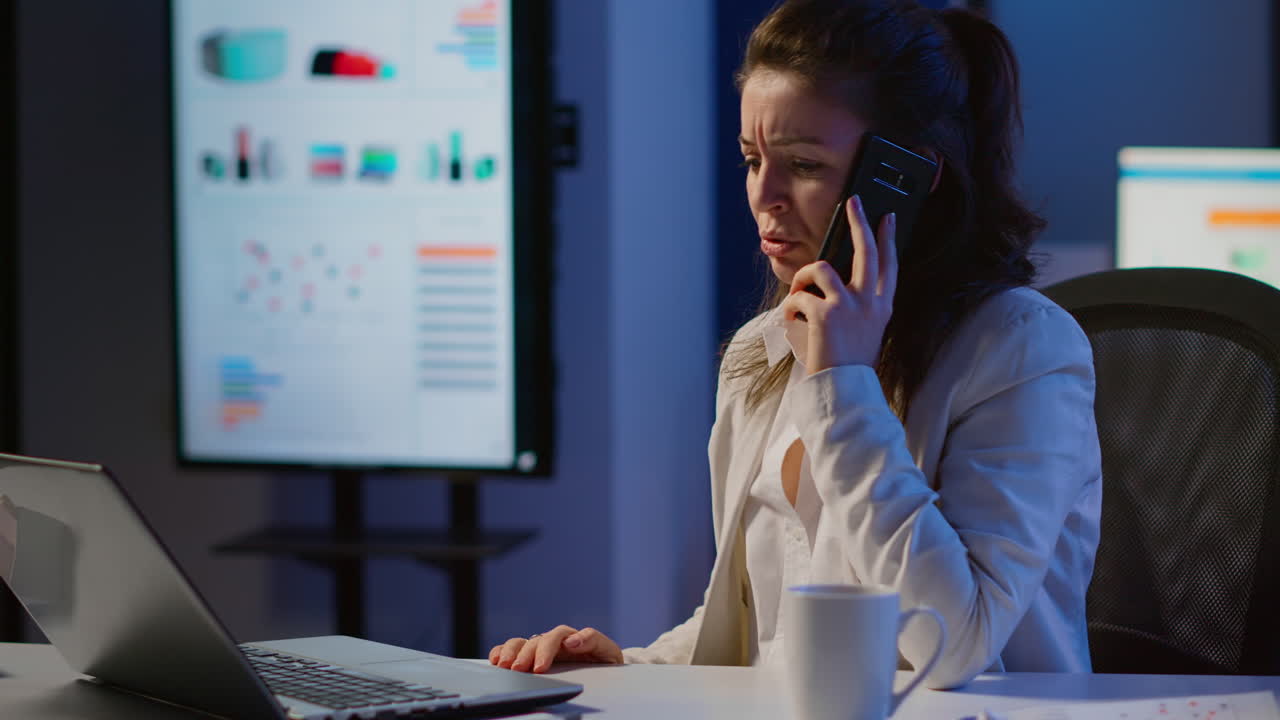 una mujer de negocios enojada haciendo una llamada telefónica en la oficina de inicio tarde en la noche.