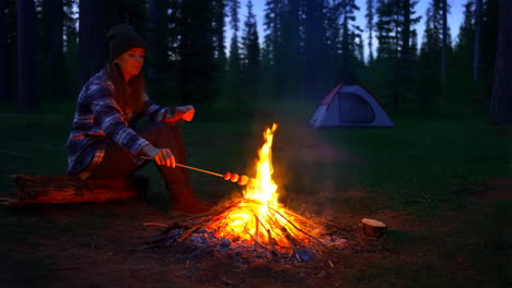 woman roasting food over campfire at night in the forest