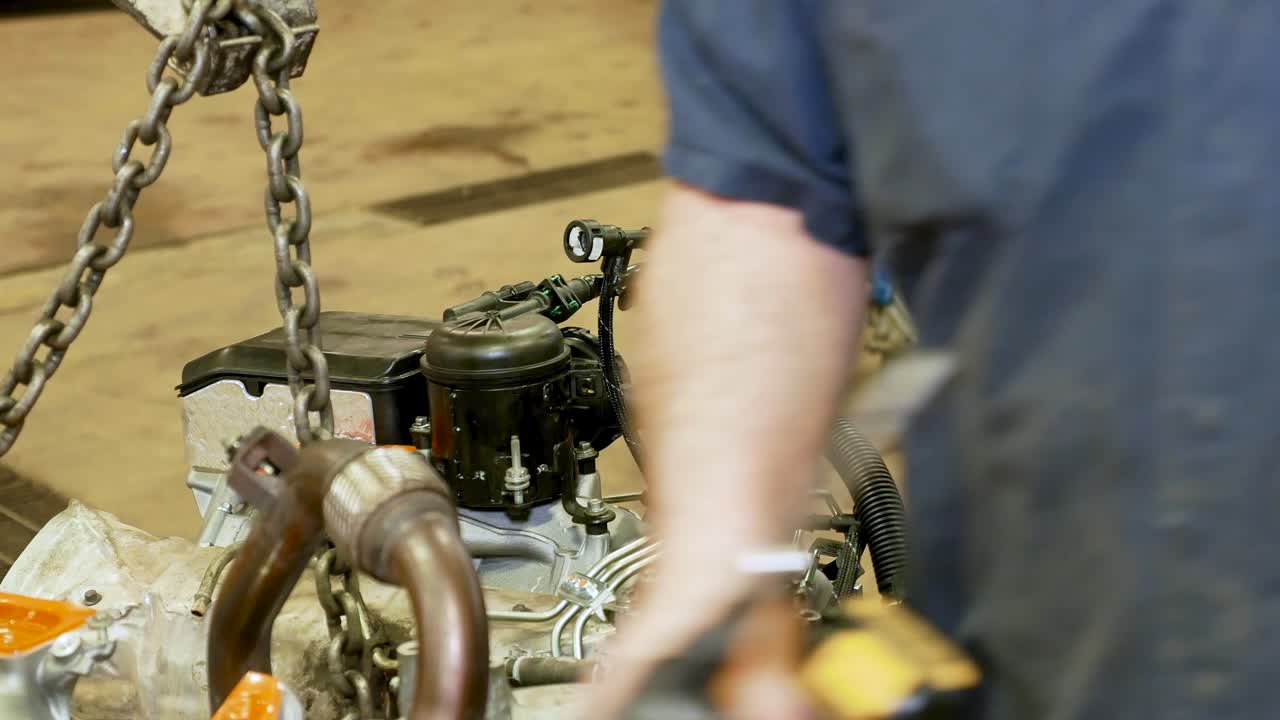 A mechanic does final prep to a new engine that is hanging off a motor crane and almost ready to go back into the vehicle