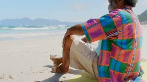 Side-view-of-thoughtful-active-senior-African-American-man-relaxing-on-beach-in-the-sunshine-4k