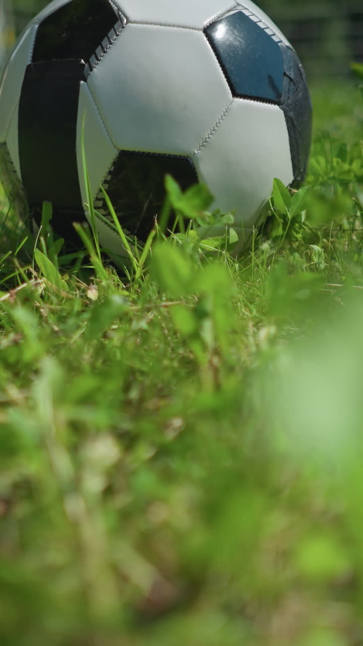 A close-up view of a soccer ball resting on a grassy field, with someone reaching down to pick it up