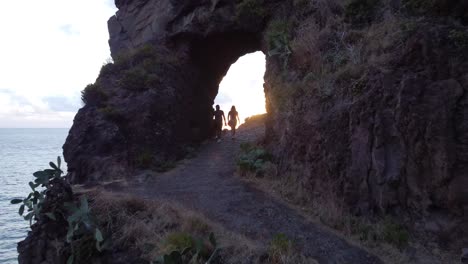 people on hiking trail under natural rock arch on island coast of madeira, portugal