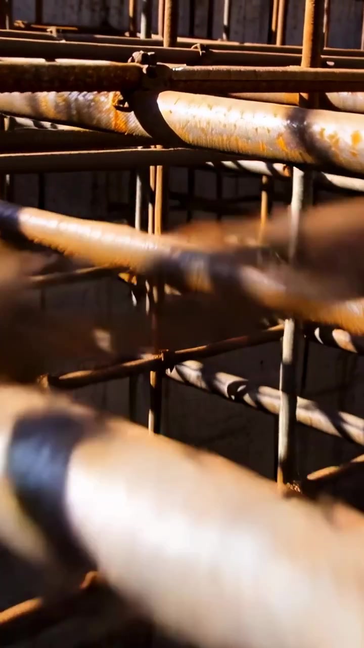 Video verticale: Telecamera in panoramica che scorre in avanti attraverso un cortile illuminato dal sole, mostrando tubi arrugginiti e morsetti.