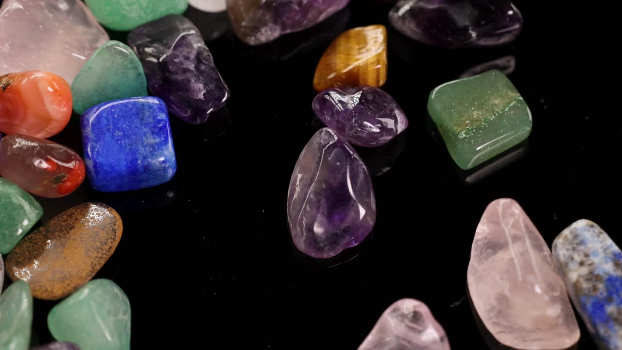 Pietre chakra colorate disposte su una superficie nera, che evidenziano le loro tonalità vivaci e le texture levigate sotto una luce soffusa.