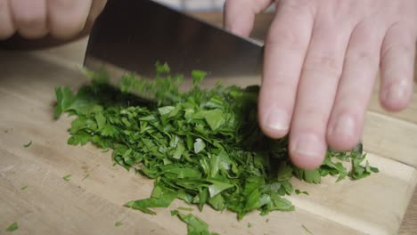 un chef corta perejil plano con un cuchillo en una tabla de cortar