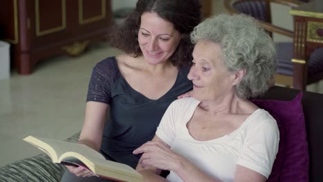 Daughter-and-mother-reading-book,-talking,-old-woman-surprised