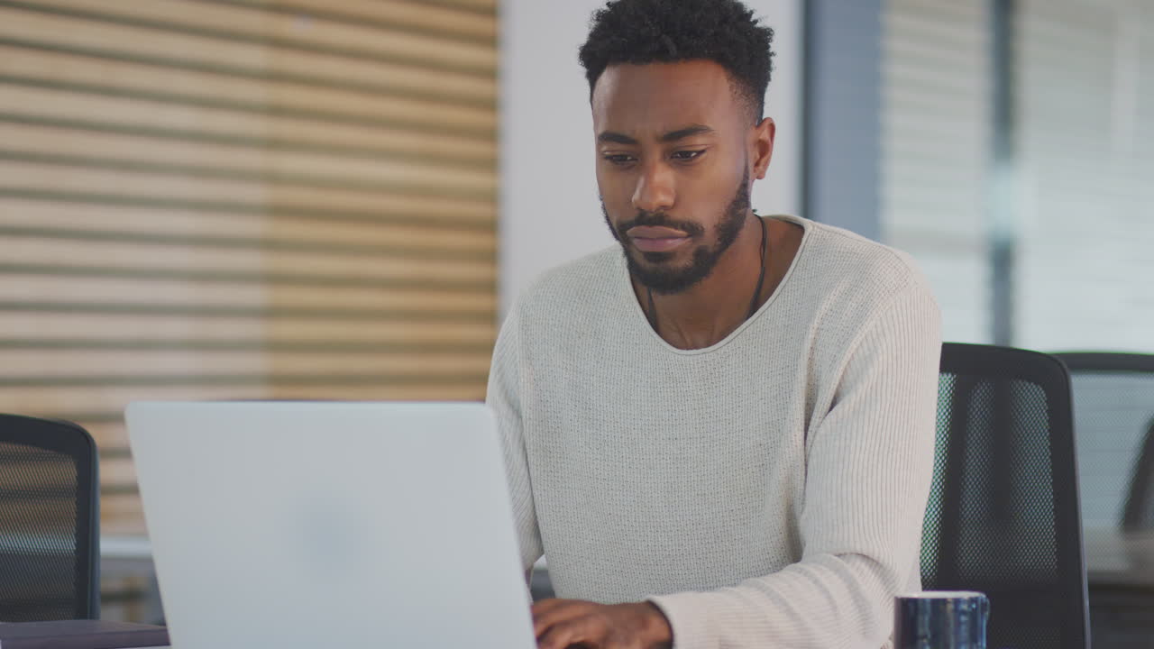 Tired Young Businessman Working Late Sitting At Desk With Laptop In Modern Open Plan Office