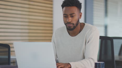 Un-Joven-Empresario-Cansado-Trabajando-Hasta-Tarde-Sentado-En-Un-Escritorio-Con-Una-Computadora-Portátil-En-Una-Oficina-Moderna-Y-Abierta