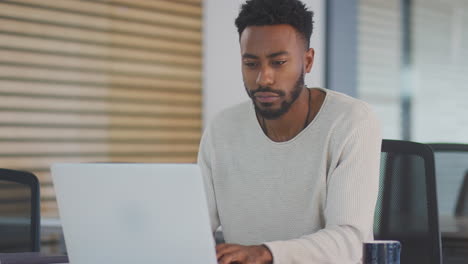 tired young businessman working late sitting at desk with laptop in modern open plan office