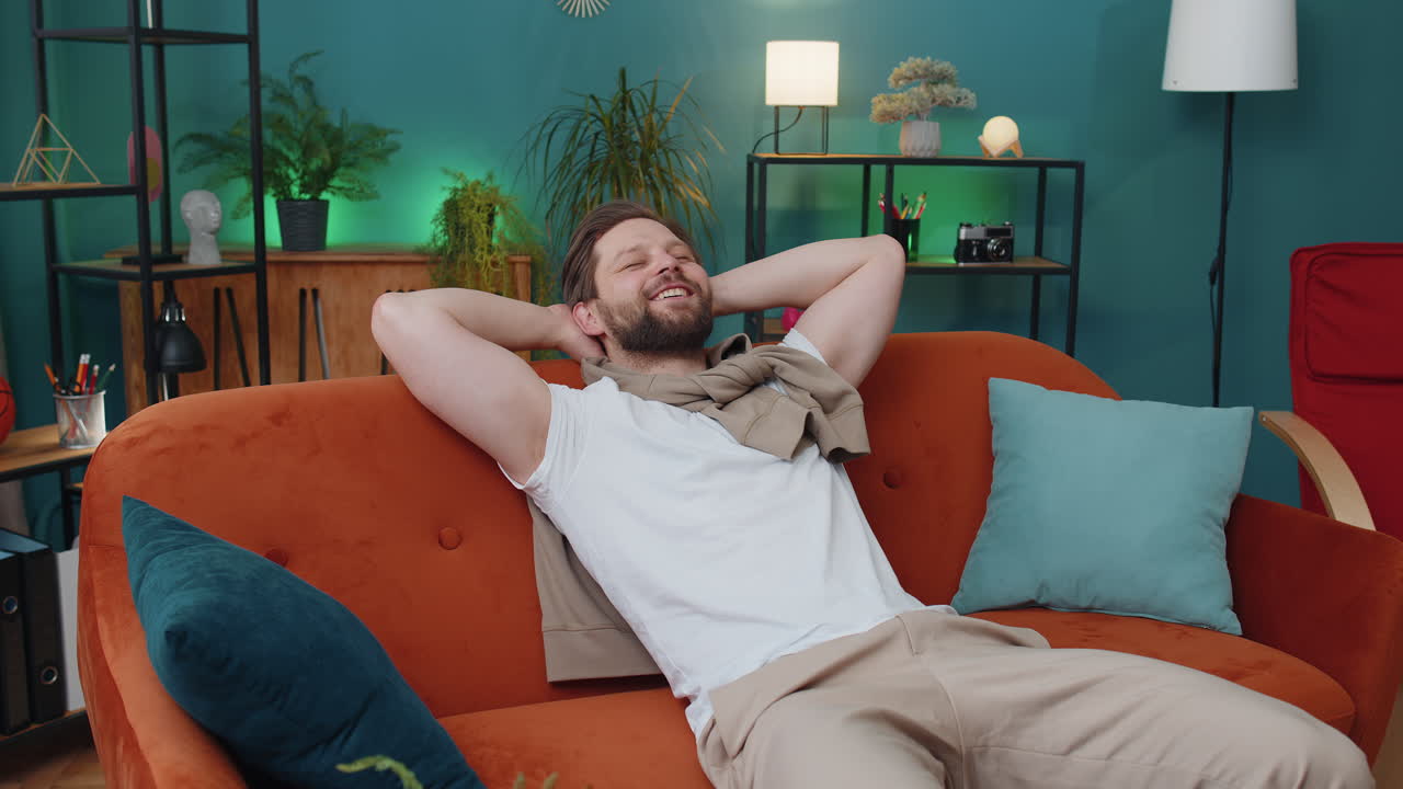 Tired young man lying down on comfortable couch taking a rest daytime nap relaxing falling asleep