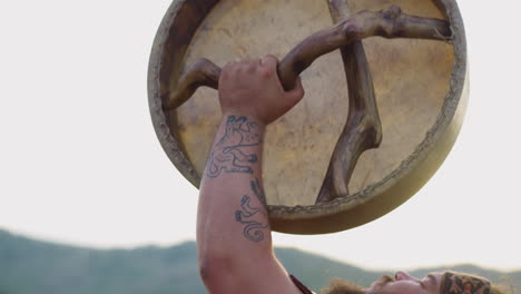 hombre gordo con tatuajes en el brazo levanta el tambor chamánico