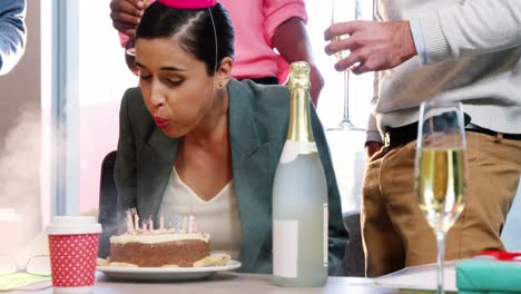 mujer de negocios soplando velas de cumpleaños con colegas