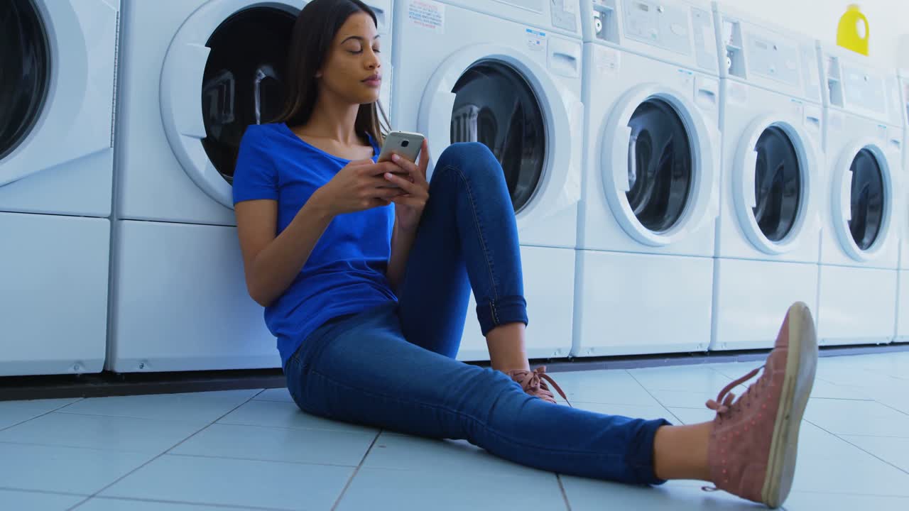 Woman using mobile phone at laundromat 4k