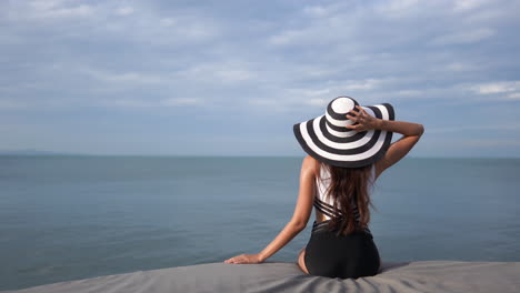 Young-slim-woman-in-bathing-suit-and-hat-looks-out-at-sea-and-scans-the-horizon