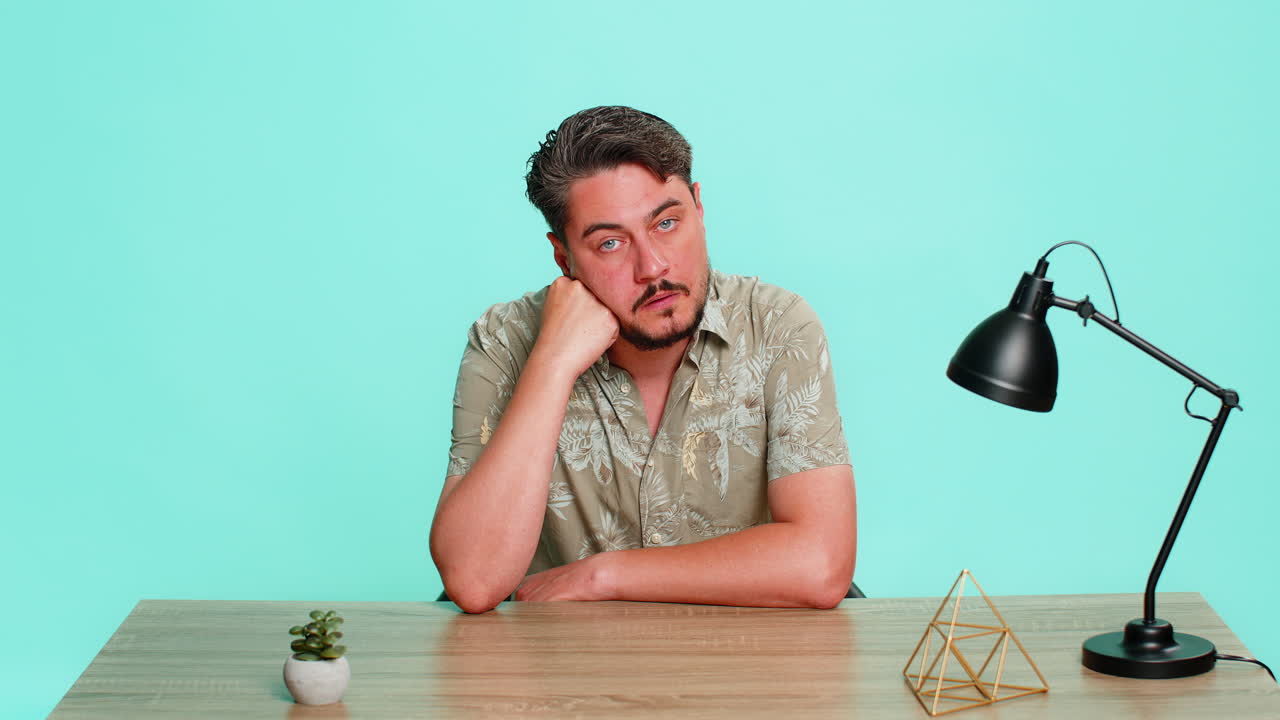 Man sitting at table supporting head with hand staring blankly feeling emotional burnout and apathy