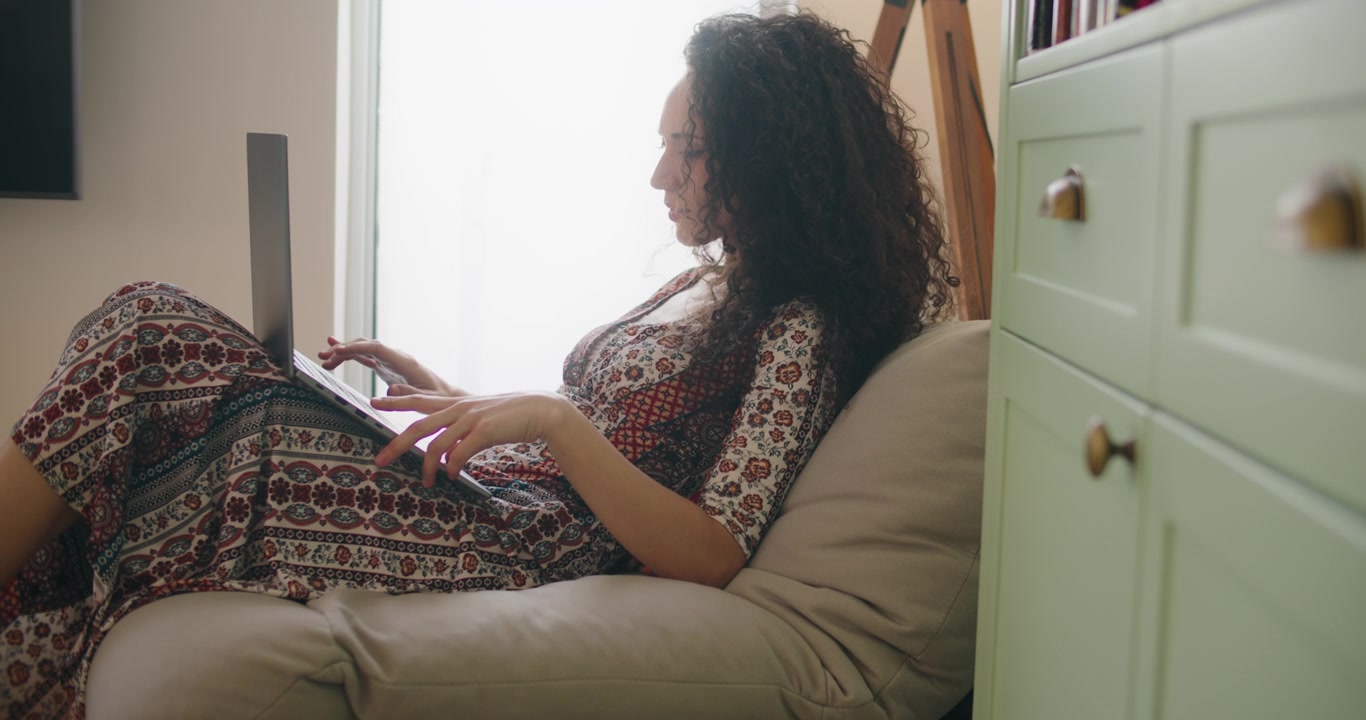 Young Woman Working on Laptop While Relaxing on Bean Bag Chair