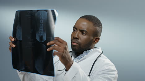 Close-Up-Of-The-Young-Man-Doctor-Or-Intern-Holding-X-Ray-Copy-And-Studying-It-Carefully-On-The-Grey-Background