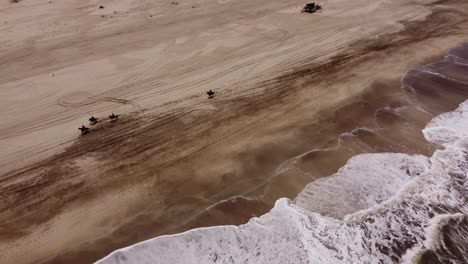 people riding horses galloping on beach washed by ocean big waves