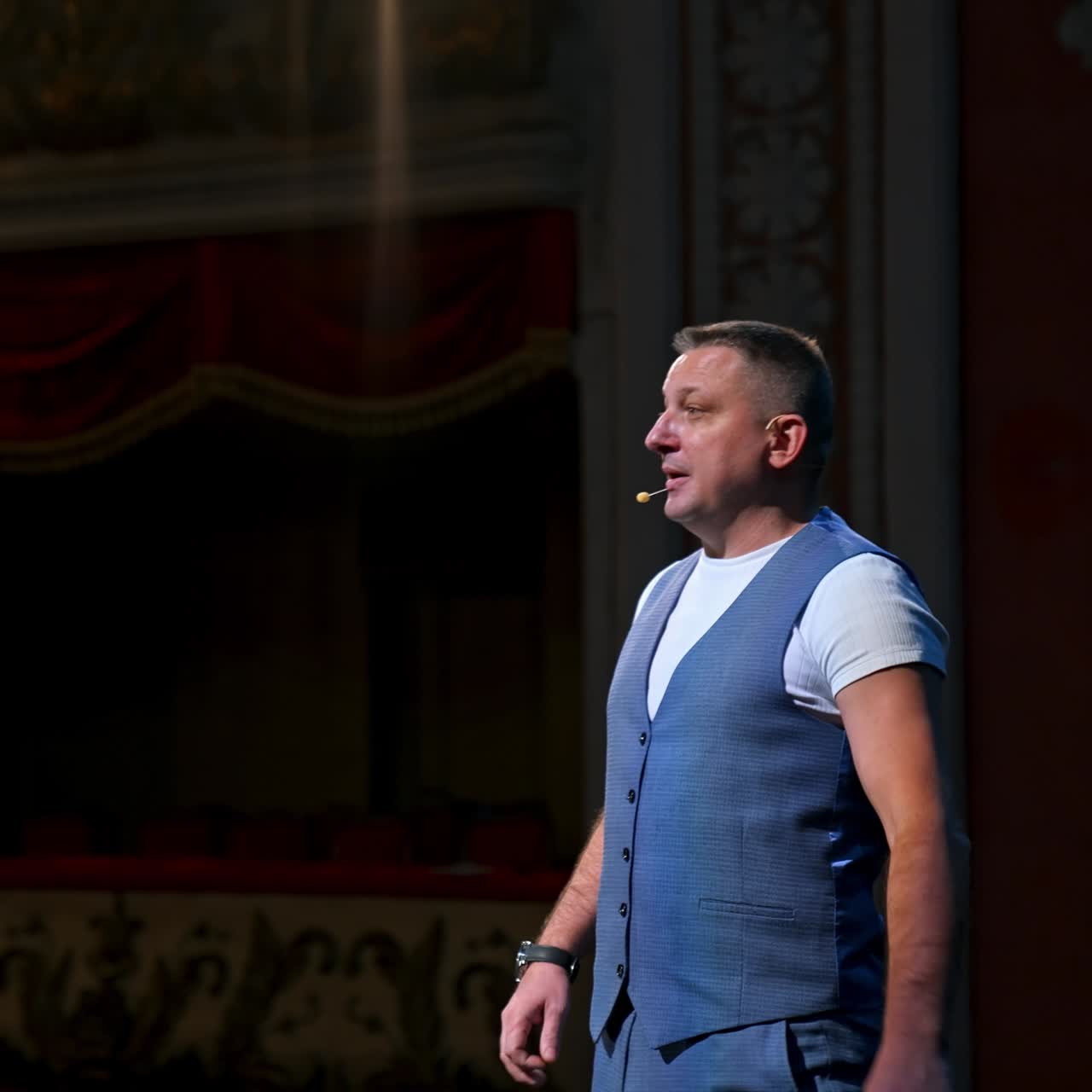 Presentatore in abito grigio sul palco. Attore maschio inizia la sua esibizione in teatro. Ritratto di un comico in piedi sul palco che parla
